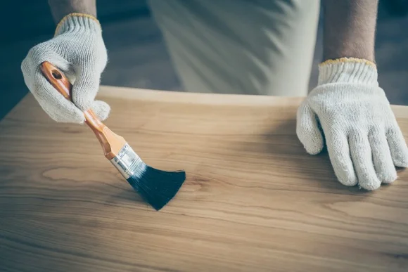 Person trägt Lack auf Holztisch auf